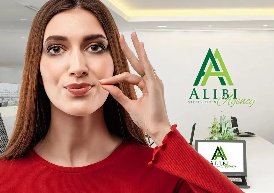 Eine Frau in der Alibiagentur zeigt eine Geste mit dem Finger, das Geheimnis bedeutet.